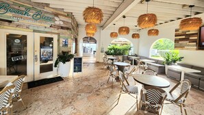 A beach-themed cafe with a wooden facade, outdoor seating, and hanging wicker lamps.