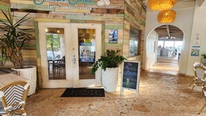 A beach-themed cafe with a wooden facade, a sign reading "The Beach Bar," and a stone-tiled floor.