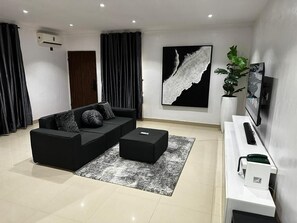Ein modernes Wohnzimmer mit einem schwarzen Sofa, einem Couchtisch, einem großen abstrakten Gemälde, einer Kühlpflanze und einer weißen Unterhaltungseinheit.