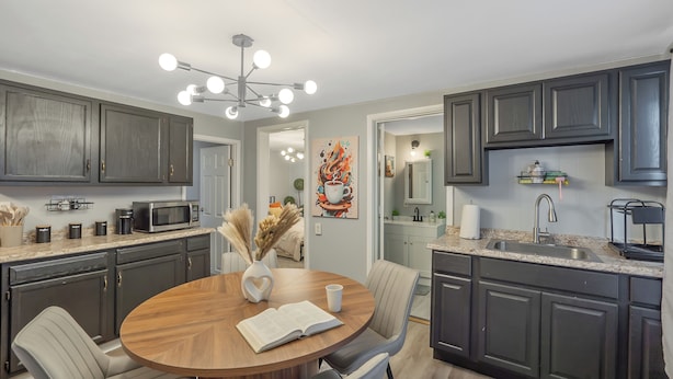 A modern kitchen with dark cabinets, a round wooden table, and a chandelier. - Stylish 2BR Syracuse Stay, Near Zoo, Museums and Downtown (Syracuse)