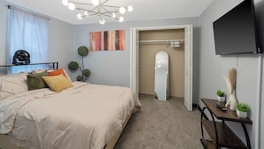 A bedroom with a bed, bedside table, mirror, and a TV mounted on the wall. - Stylish 2BR Syracuse Stay, Near Zoo, Museums and Downtown (Syracuse)