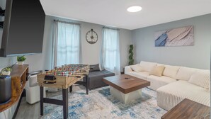 A living room with a foosball table, a sofa, a coffee table, and a TV mounted on the wall. - Stylish 2BR Syracuse Stay, Near Zoo, Museums and Downtown (Syracuse)