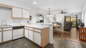 A modern kitchen with a central island, a dining area with a table and chairs, and a view of the outdoors through a sliding glass door.