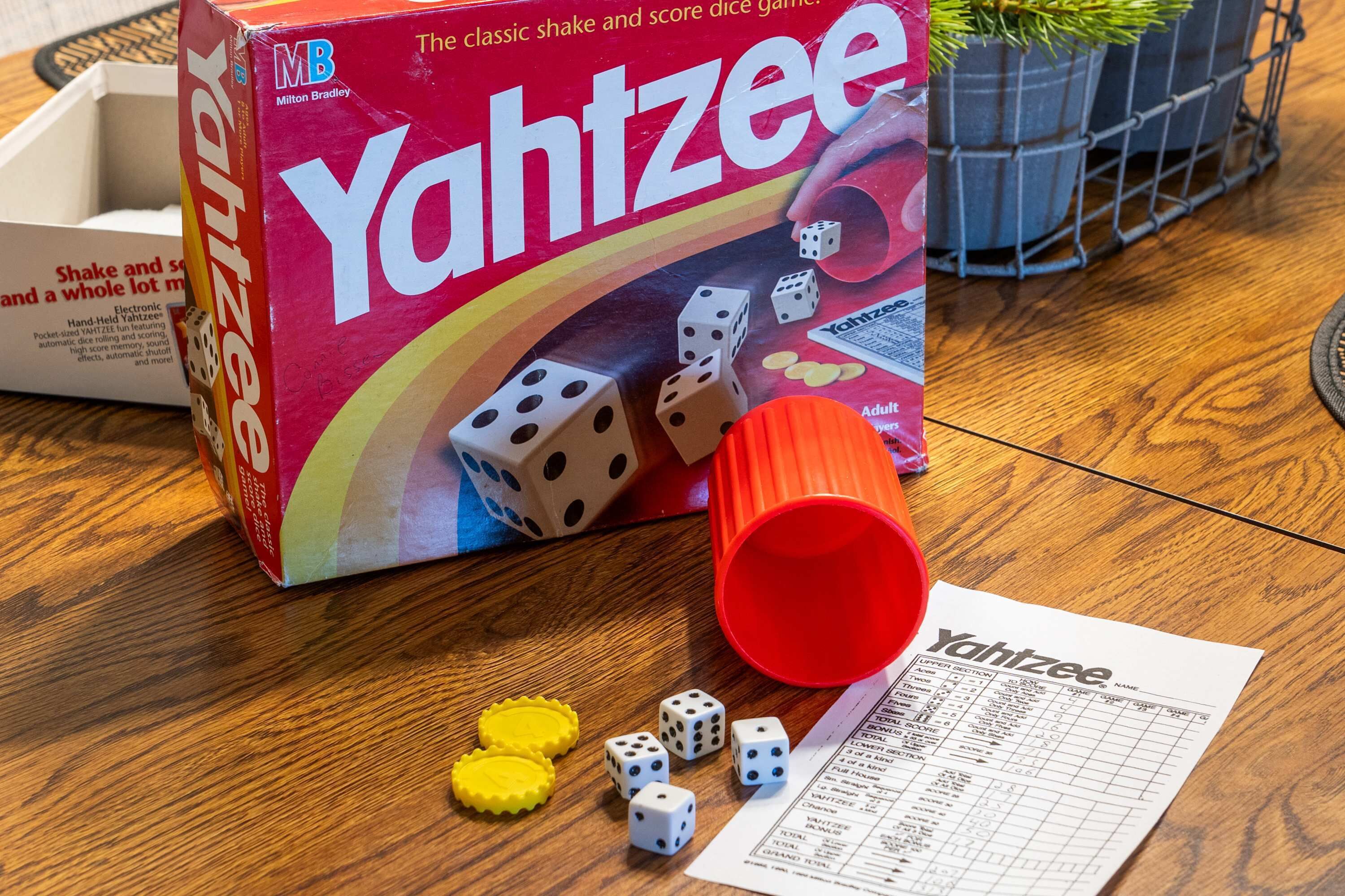 A Yahtzee game box, dice, and a score sheet on a wooden table.