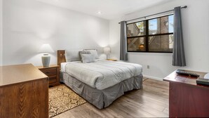 A bedroom with a large bed, bedside tables, a desk, and a window with curtains.