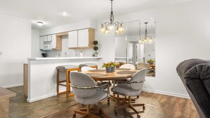 A modern kitchen with white cabinets, a central island, and a dining area with a wooden table and four chairs.