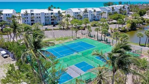 A resort with multiple white buildings, a tennis court, and a body of water. - Captiva Beachfront Condo 2322 | Direct Gulf Front | Pool, Tennis & Pickleball (Captiva)