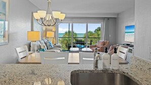 A modern hotel room with a kitchen area, dining space, and a balcony with a view of the ocean. - Captiva Beachfront Condo 2322 | Direct Gulf Front | Pool, Tennis & Pickleball (Captiva)