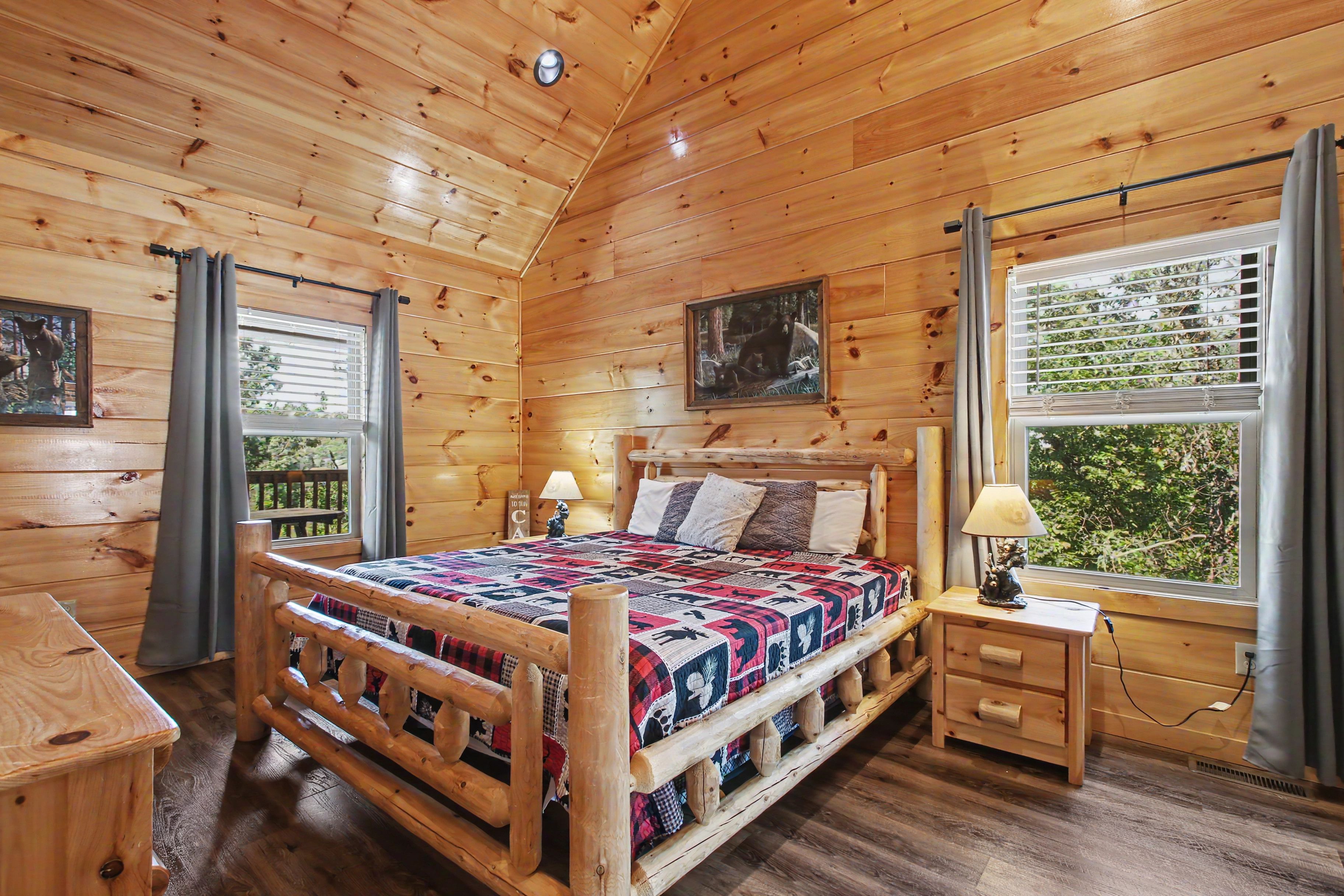 A wooden cabin bedroom with a bed, bedside table, lamp, and a window with blinds.