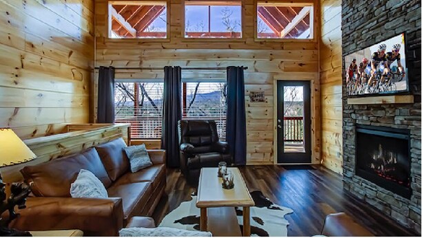 L’intérieur d’une cabane en rondins, avec une cheminée, un canapé en cuir et une vue sur les montagnes à travers de grandes fenêtres.