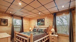 Une chambre à coucher de style cabane en bois, avec un grand lit, deux tables de chevet et une fenêtre avec des rideaux.