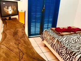 A room with a television on a wooden stand, a bed with a zebra print cover, and a blue door with shutters.