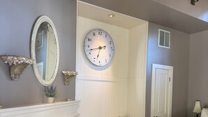 A bedroom with a fireplace, a large wall clock, a bench, and a bed.