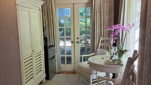 A room with a white cabinet, a dining table with chairs, and a window with curtains.