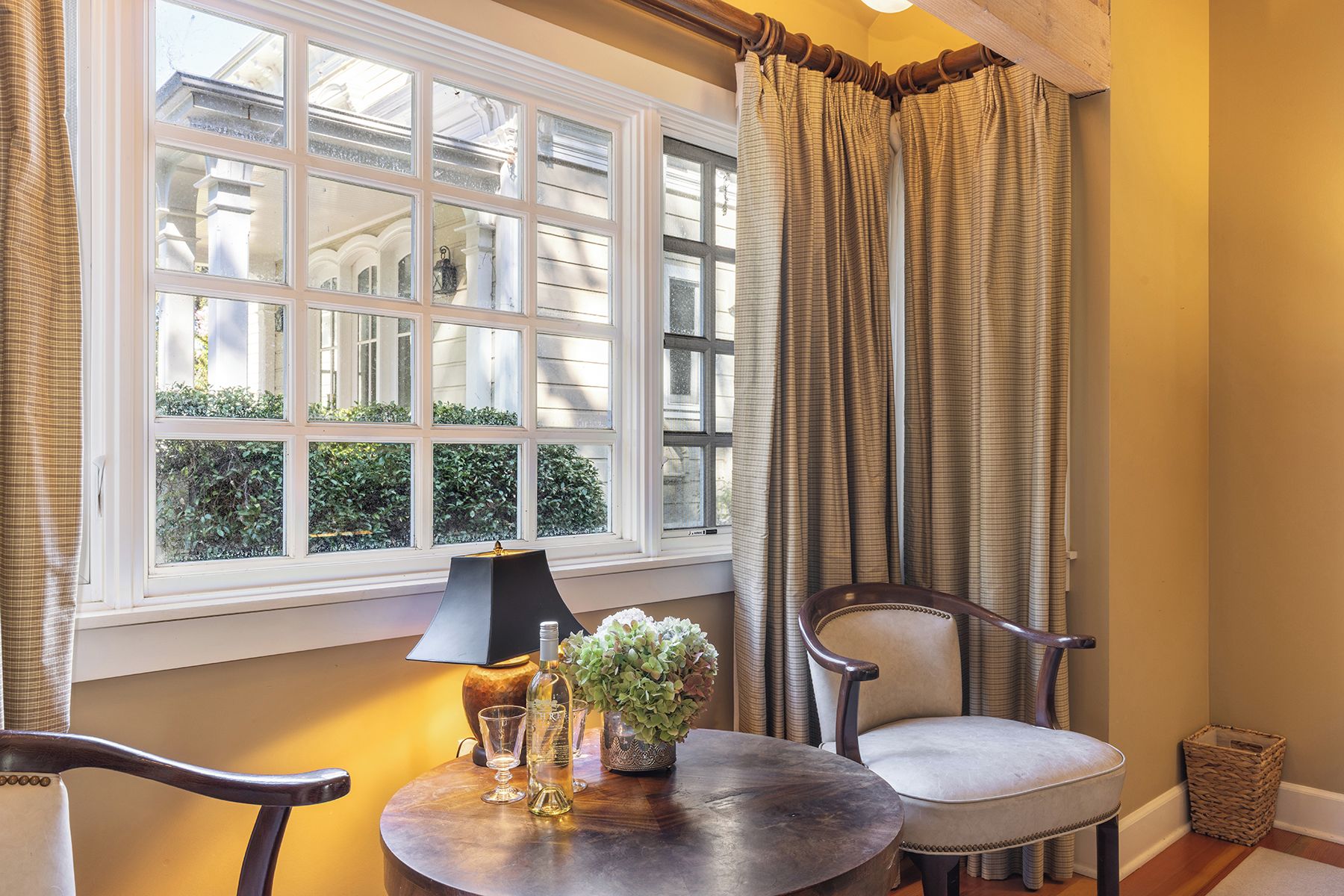 A room with a large window, a table with a lamp, chairs, and a small plant.