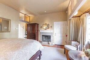 Un dormitorio con cama, chimenea, una silla y un espejo.