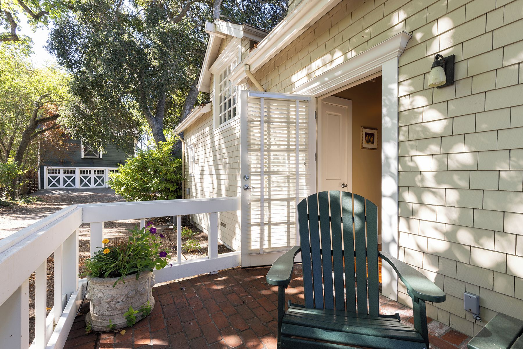 A porch with a green Adirondack chair, a white railing, and a potted plant with flowers.