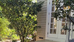 A patio with a green table and a bench, a small tree, and a house with a white door and steps.