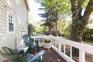 A porch with two green Adirondack chairs, a white railing, and a potted plant. - Cedar Mansion Estate & Bungalows - London Suite (Sonoma)