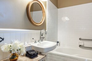 A bathroom with a white sink, a mirror, and a bathtub. - Cedar Mansion Estate & Bungalows - London Suite (Sonoma)