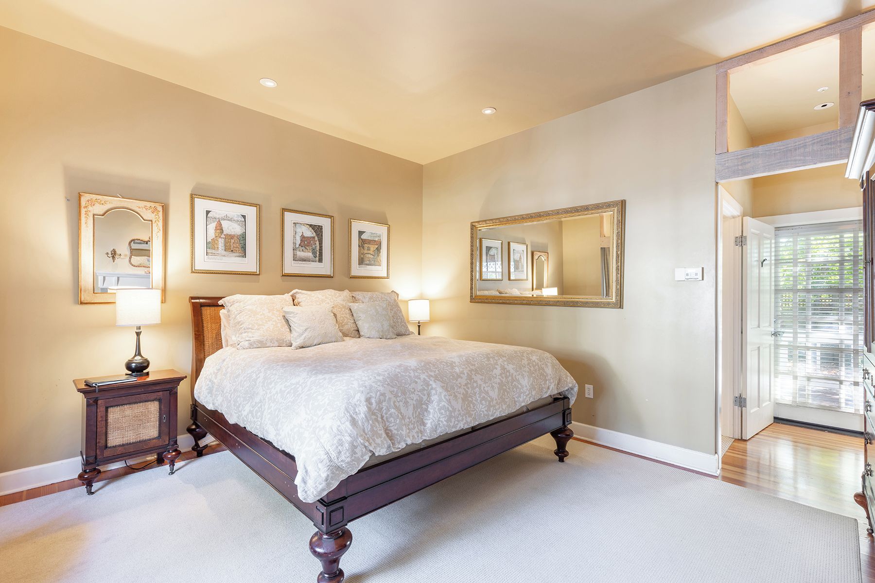 Une chambre à coucher avec un grand lit, une table de chevet, un miroir et des tableaux encadrés accrochés au mur.