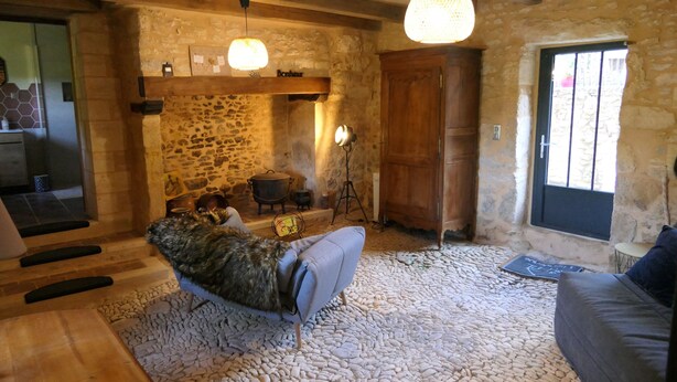 A rustic stone-walled room with a stone floor, wooden furniture, and a cozy seating area.