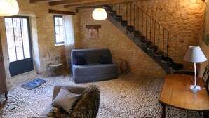 A rustic room with a stone wall, a wooden staircase, a sofa, and a table.