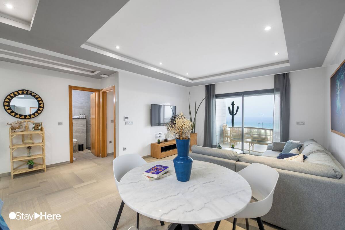 A modern living room with a round marble table, grey sofa, and a TV on the wall.