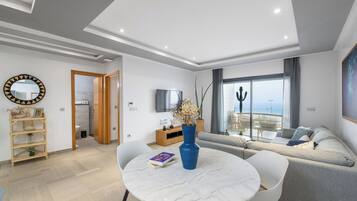 Een moderne woonkamer met een ronde marmeren tafel, een grijze bank en een televisie aan de muur.