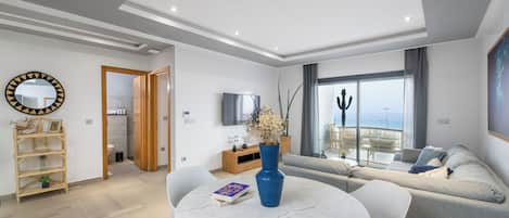 Un salon moderne avec une table ronde en marbre, un canapé gris et un téléviseur fixé au mur.