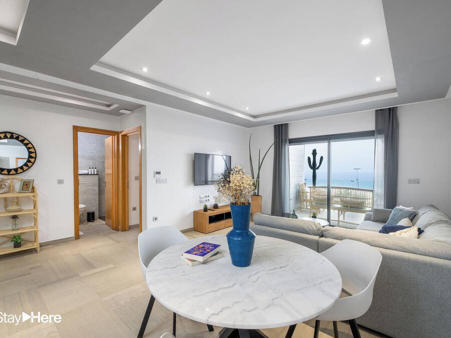 Een moderne woonkamer met een ronde marmeren tafel, een grijze bank en een televisie aan de muur.