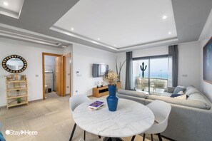 Un salon moderne avec une table ronde en marbre, un canapé gris et un téléviseur fixé au mur.
