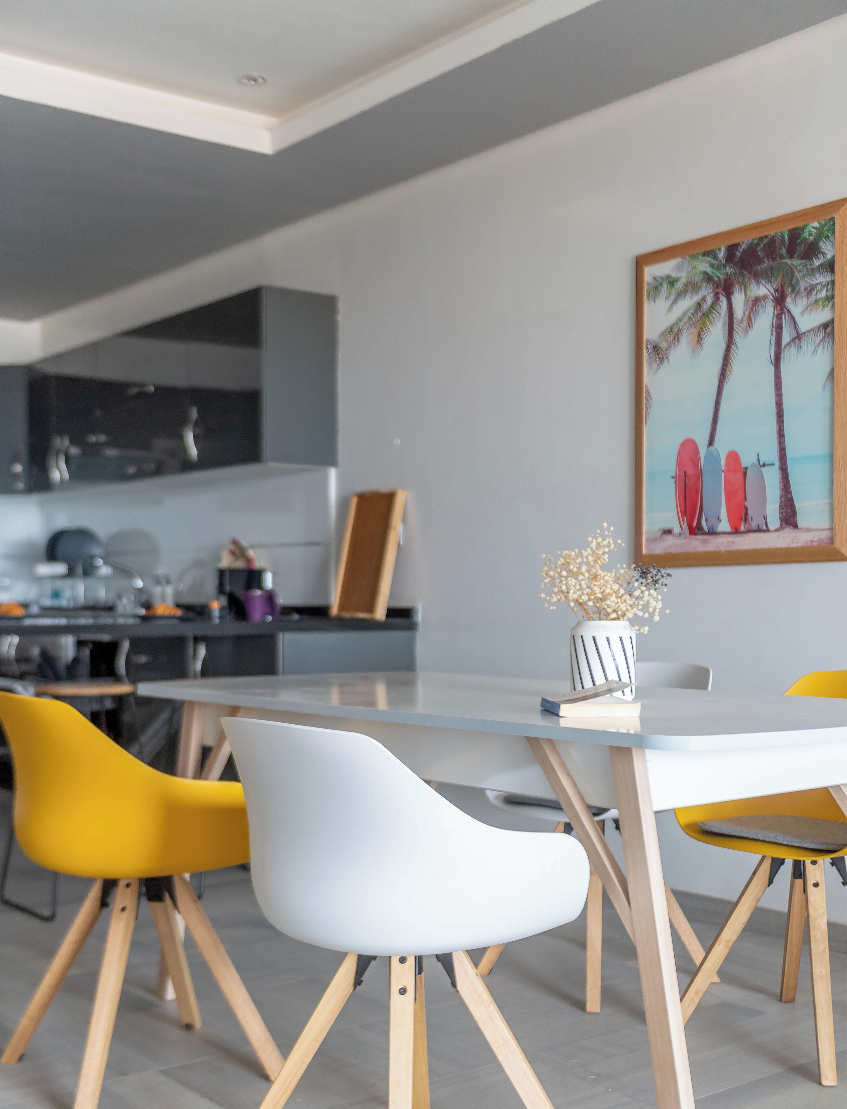 Een moderne eetruimte met een witte tafel, gele en witte stoelen en een keuken op de achtergrond.