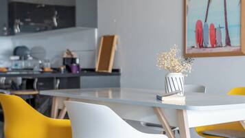 Een moderne eetruimte met een witte tafel, gele en witte stoelen en een keuken op de achtergrond.