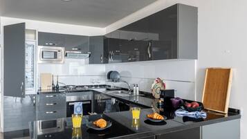 Een moderne keuken met een ingebouwde oven, magnetron en kookplaat. Er is een ontbijt klaargezet met croissants, sap en een fruitschaal.