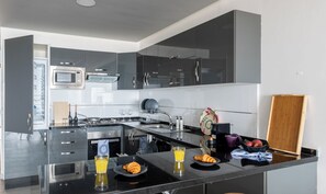 A modern kitchen with a built-in oven, microwave, and stove. There is a breakfast setup with croissants, juice, and a bowl of fruit. - Stayhere - Agadir - Marina Residential Living (Inezgane)