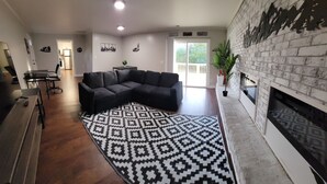 Ein Wohnzimmer mit einem Ecksofa, einem gemusterten Teppich, einem Kamin und einem Essbereich mit Tisch und Stühlen.