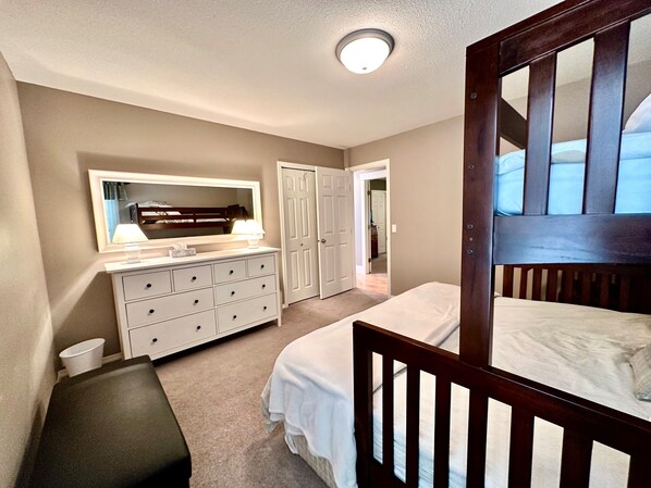 Un dormitorio con cama, cómoda, espejo y puerta que da a otra habitación.