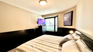 Hotellihuone, jossa on sänky, televisio, ikkuna ja taulu seinällä.