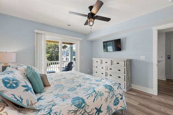 A bedroom with a bed, a ceiling fan, a TV on the wall, and a view of the outside. - Sound Dream: New Build | Pool & Hot Tub (Corolla)