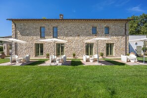 A stone building with a tiled roof, outdoor seating with umbrellas, and a well-maintained lawn.