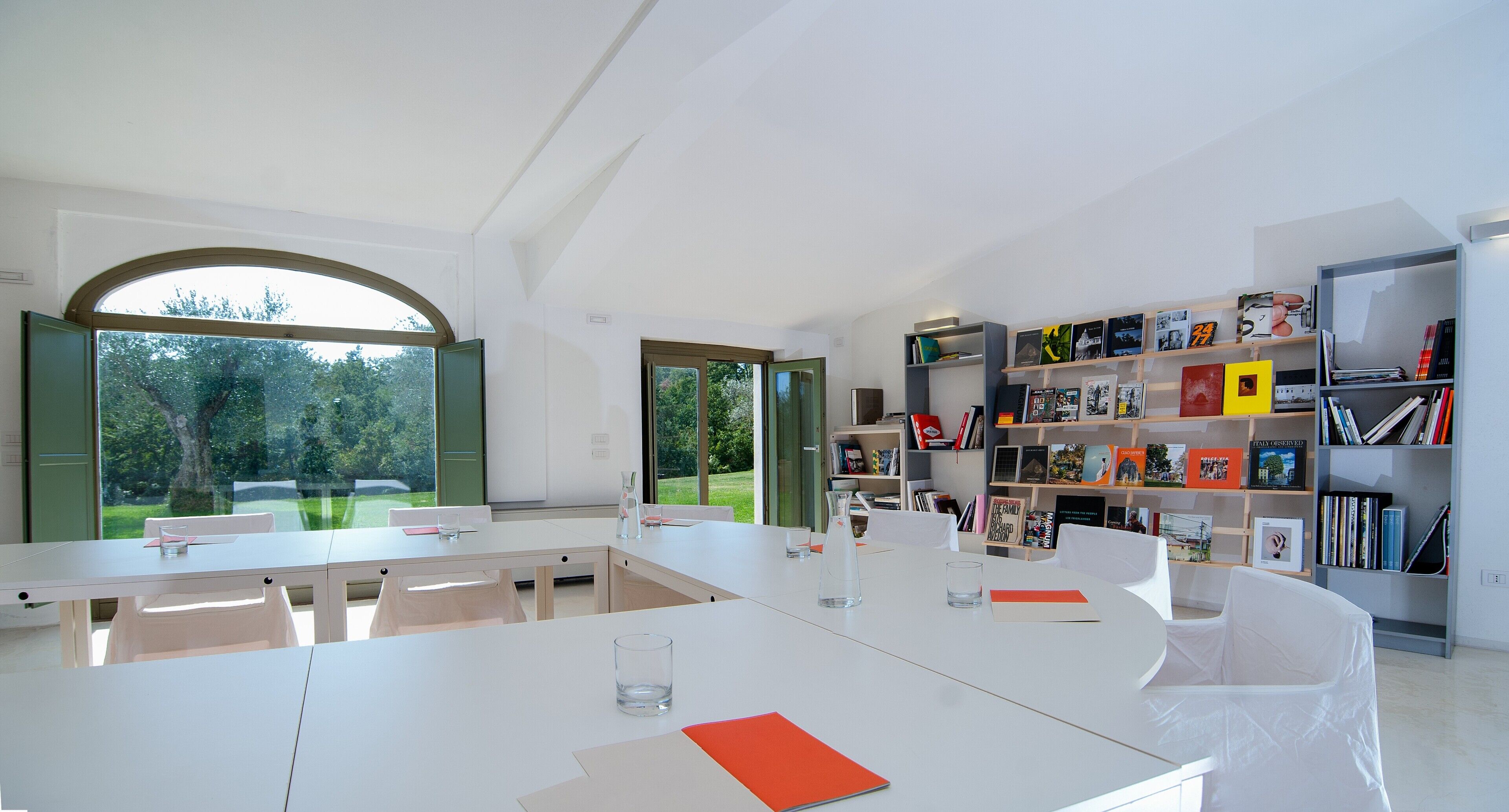 A modern library with white furniture, large windows, and a bookshelf filled with books.