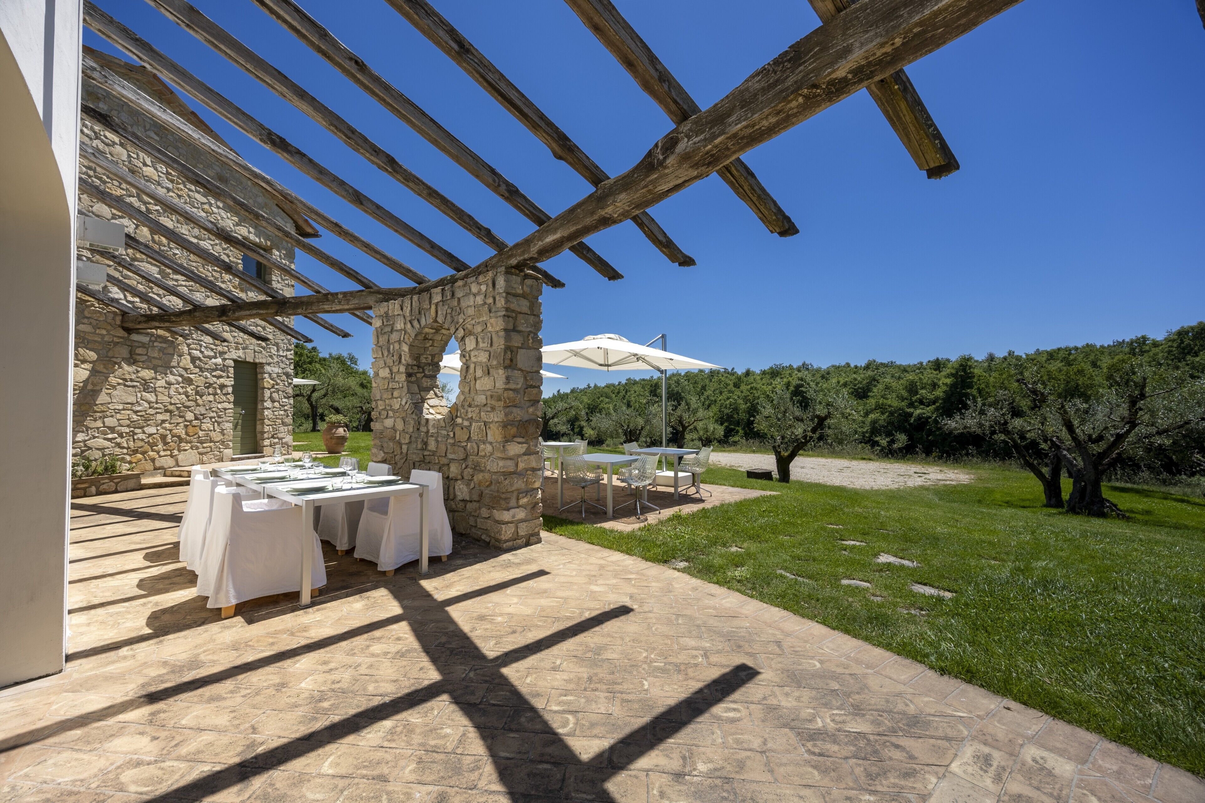 An outdoor patio with stone walls, wooden beams, and tables set for dining.