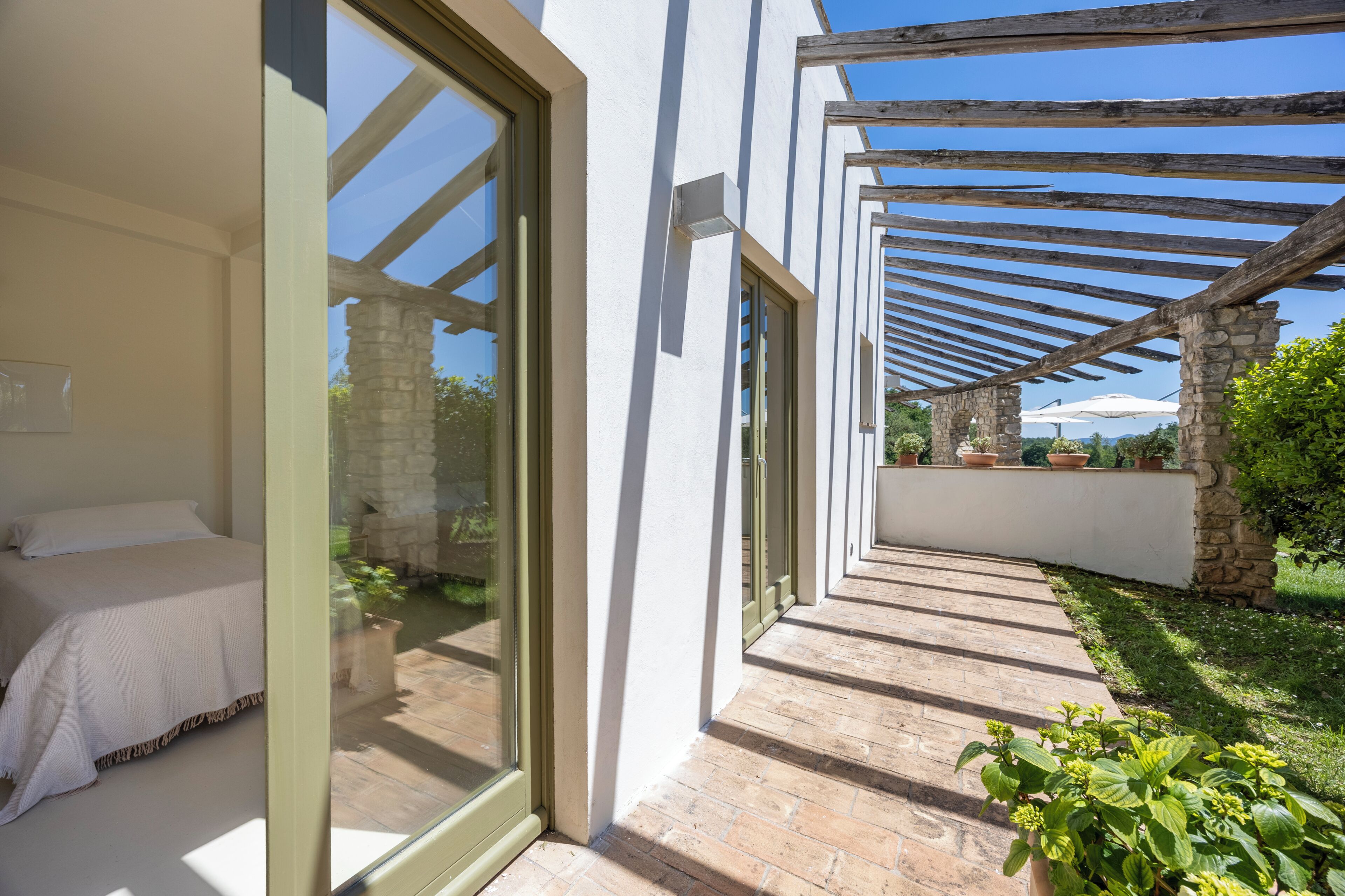 A modern bedroom with a large window, a stone wall, and a wooden pergola.