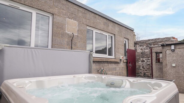 A hot tub in front of a stone building with a window and a door. - Crannoch Self Catering (Buckie)