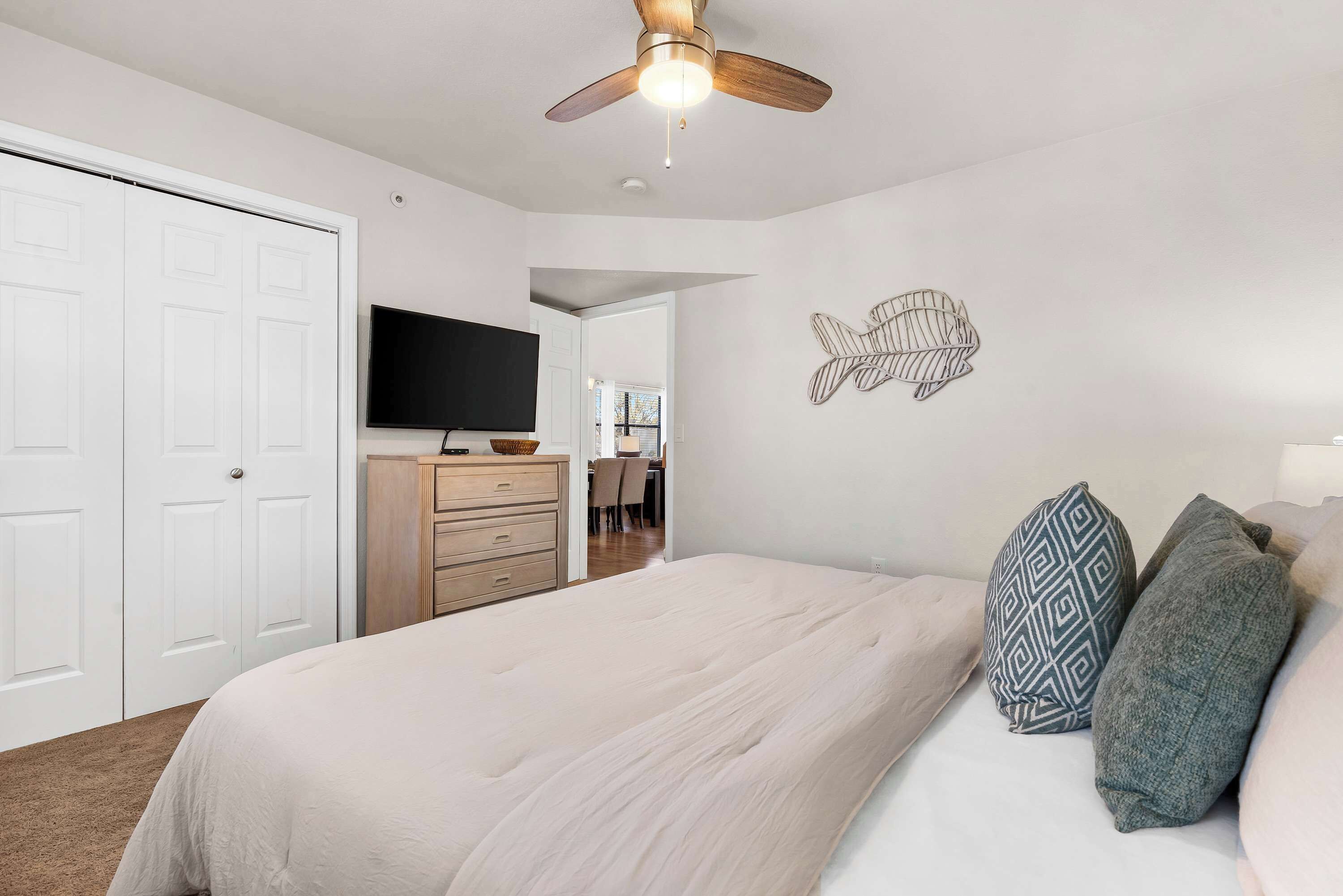 A bedroom with a bed, pillows, a ceiling fan, a TV, and a wall decoration.