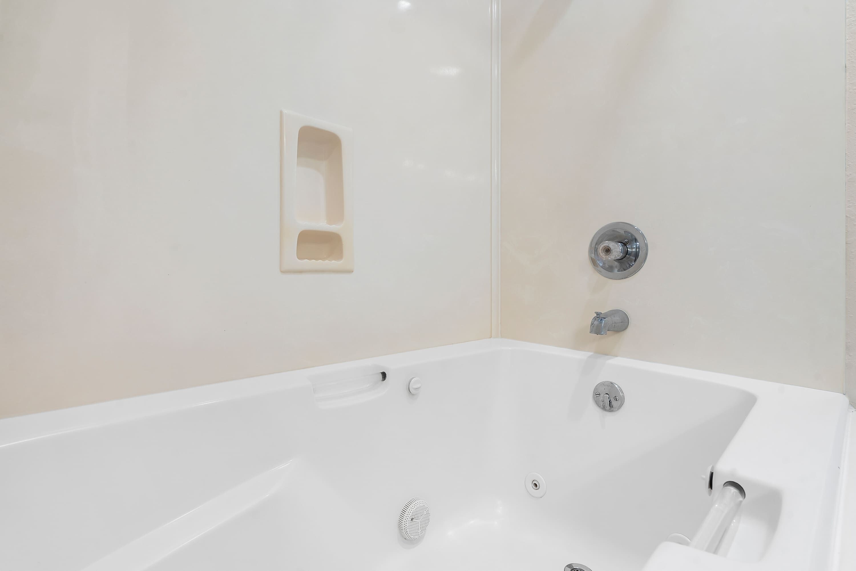 Una bañera blanca con un solo grifo y un pequeño estante.
