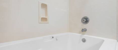 Una bañera blanca con un solo grifo y un pequeño estante.