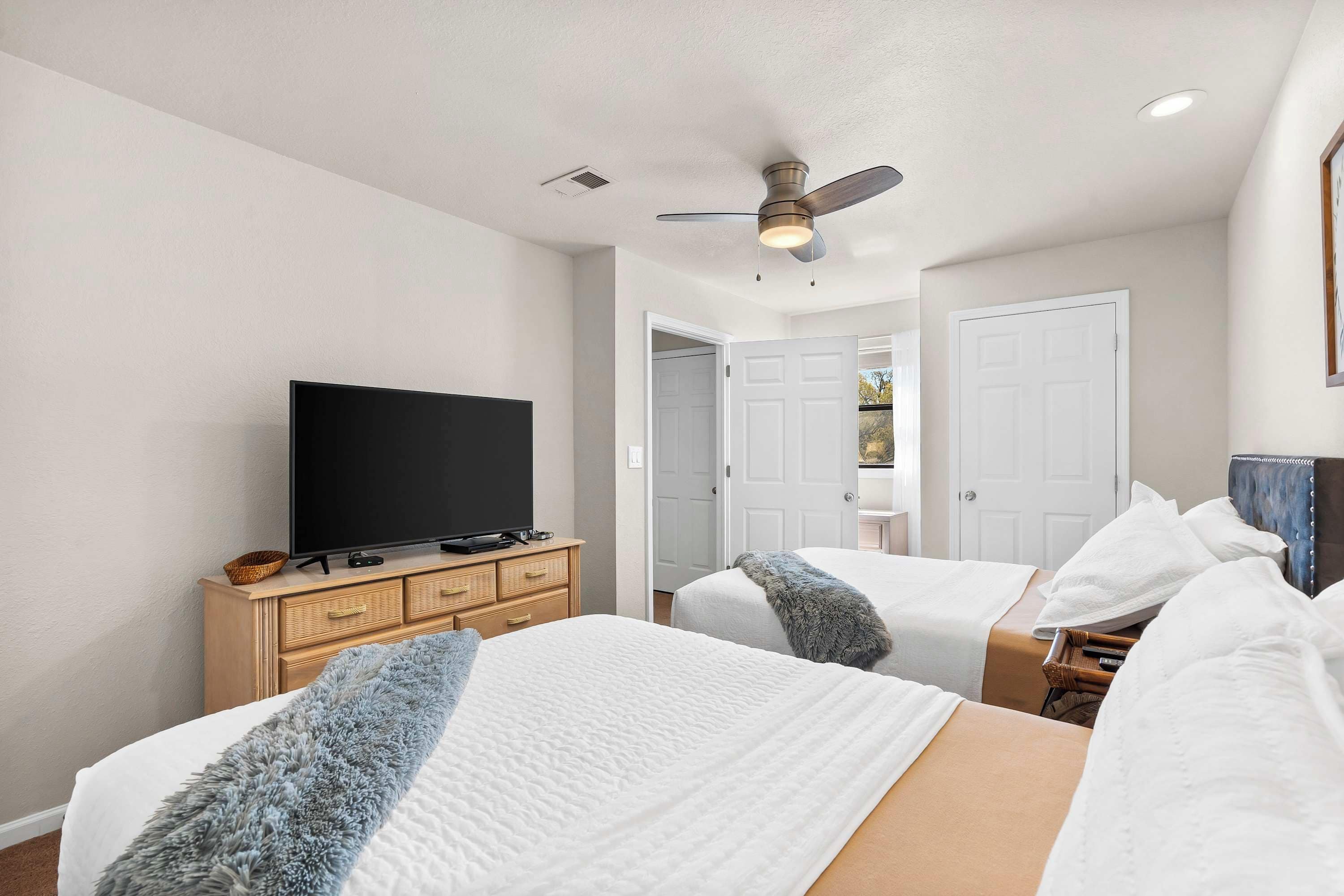A bedroom with two beds, a television on a wooden dresser, and a ceiling fan.