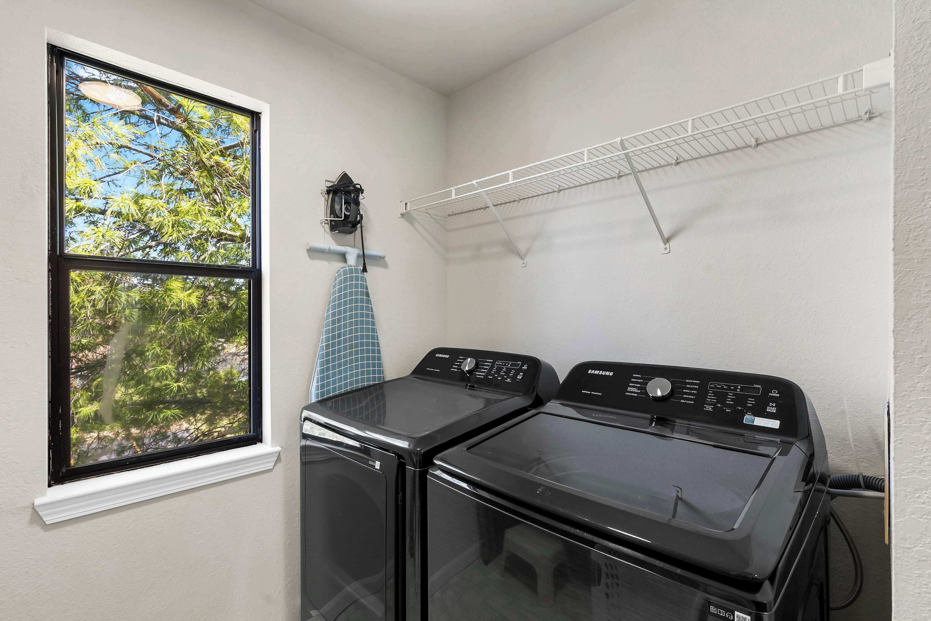 A laundry room with two black washing machines, a window with a view of trees, and a drying rack on the wall.